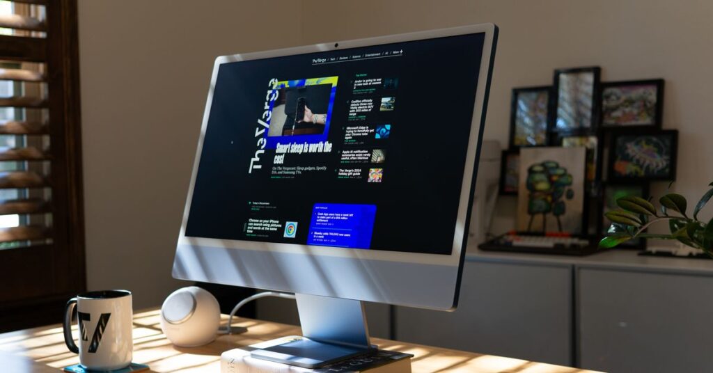 A blue all-in-one computer on a sun-lit bamboo desk. It is sitting on a hardcover book called “the unreal and the real” by Ursula K LeGuin.