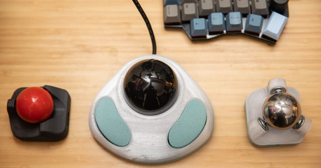 A man using a split keyboard with a trackball between the two halves. It features a large, shiny metal ball bearing.