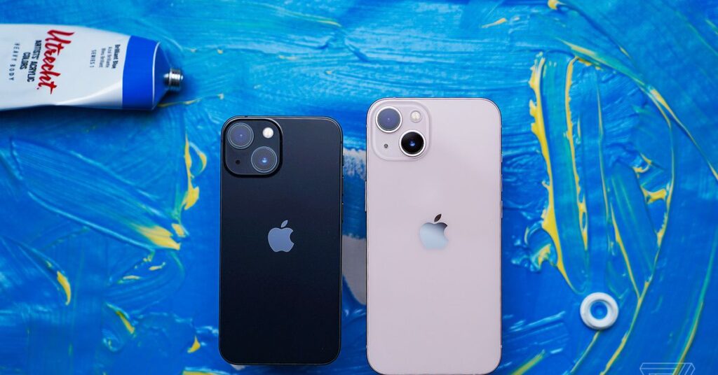 Photo of an iPhone 13 Mini next to a regular-sized iPhone 13 on a blue painted background.