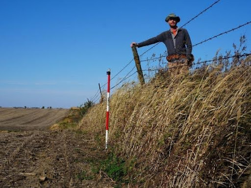 Isaac Larsen stands near a drop-off that separates native remnant prairie from farmland in Iowa