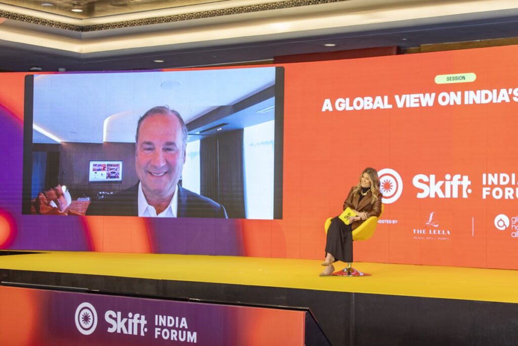 A woman sitting on a stage interviewing a man on a remote feed