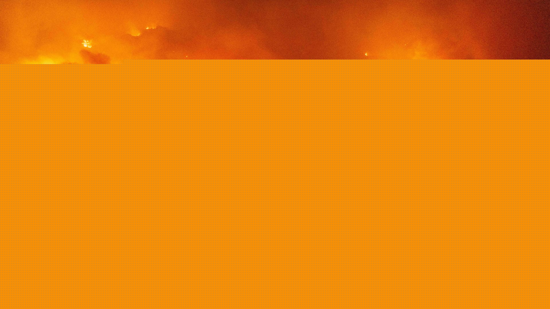 a firefighter wearing gear stands on a hill looking out at a large wildfire