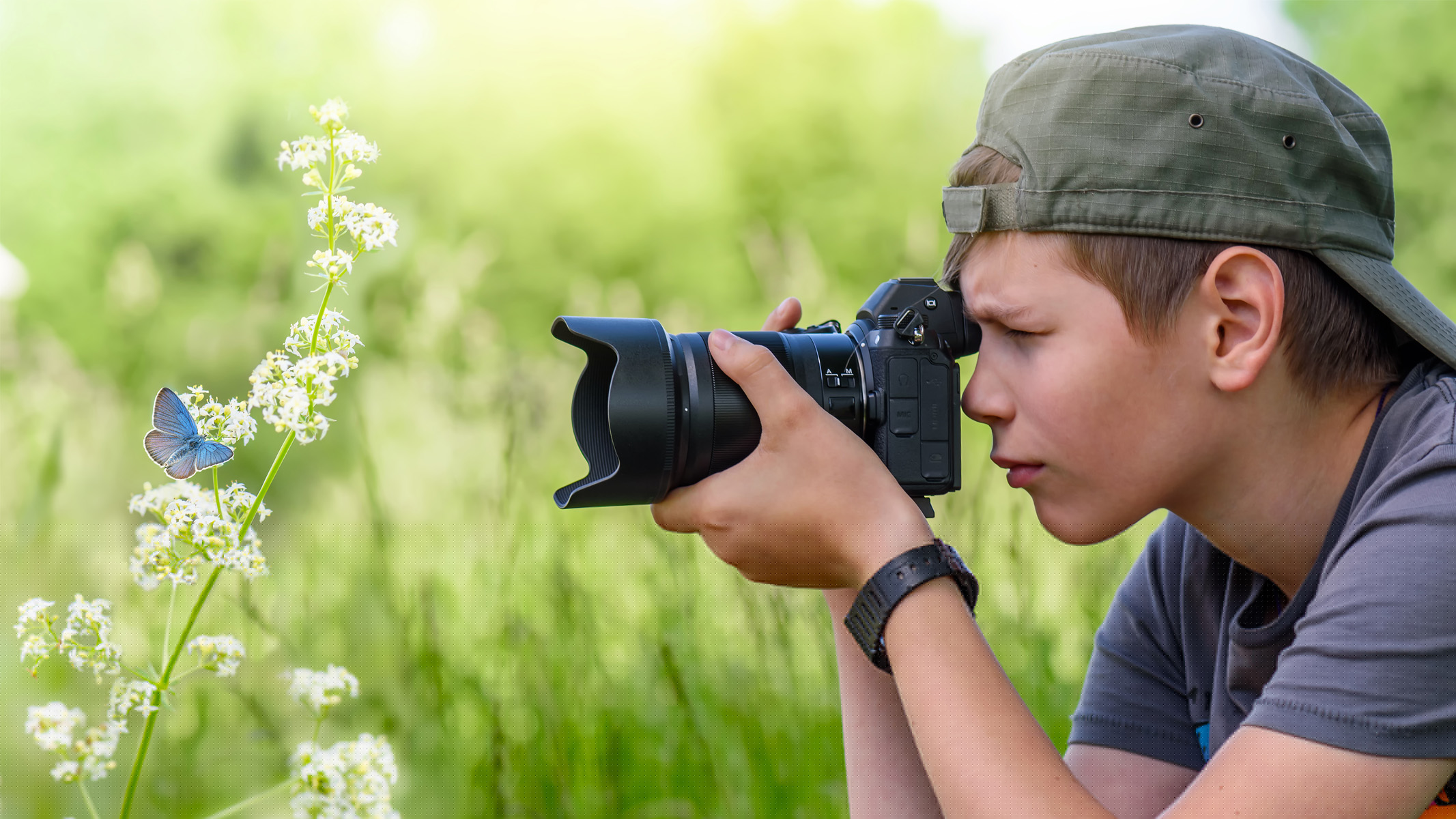 boy photographing a flower and butterfly in a field