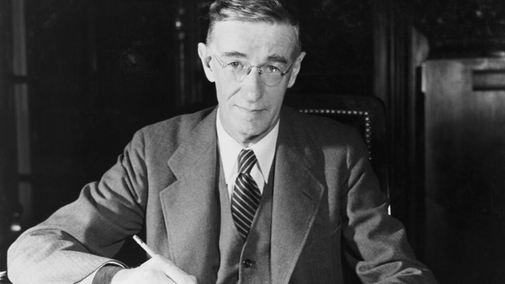 A black and white portrait of Dr. Vannevar Bush sitting at his desk